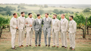 Groomsmen in slim-fit, light spring suits pose by a vineyard, offering a polished, fresh look for an outdoor wedding.